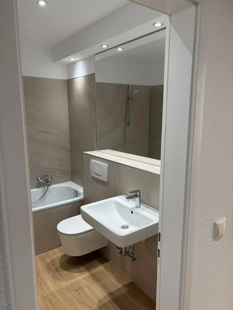 Modernisiertes Bad mit Badewanne, Waschtisch, großem Spiegel und ruhigen Wandflächen