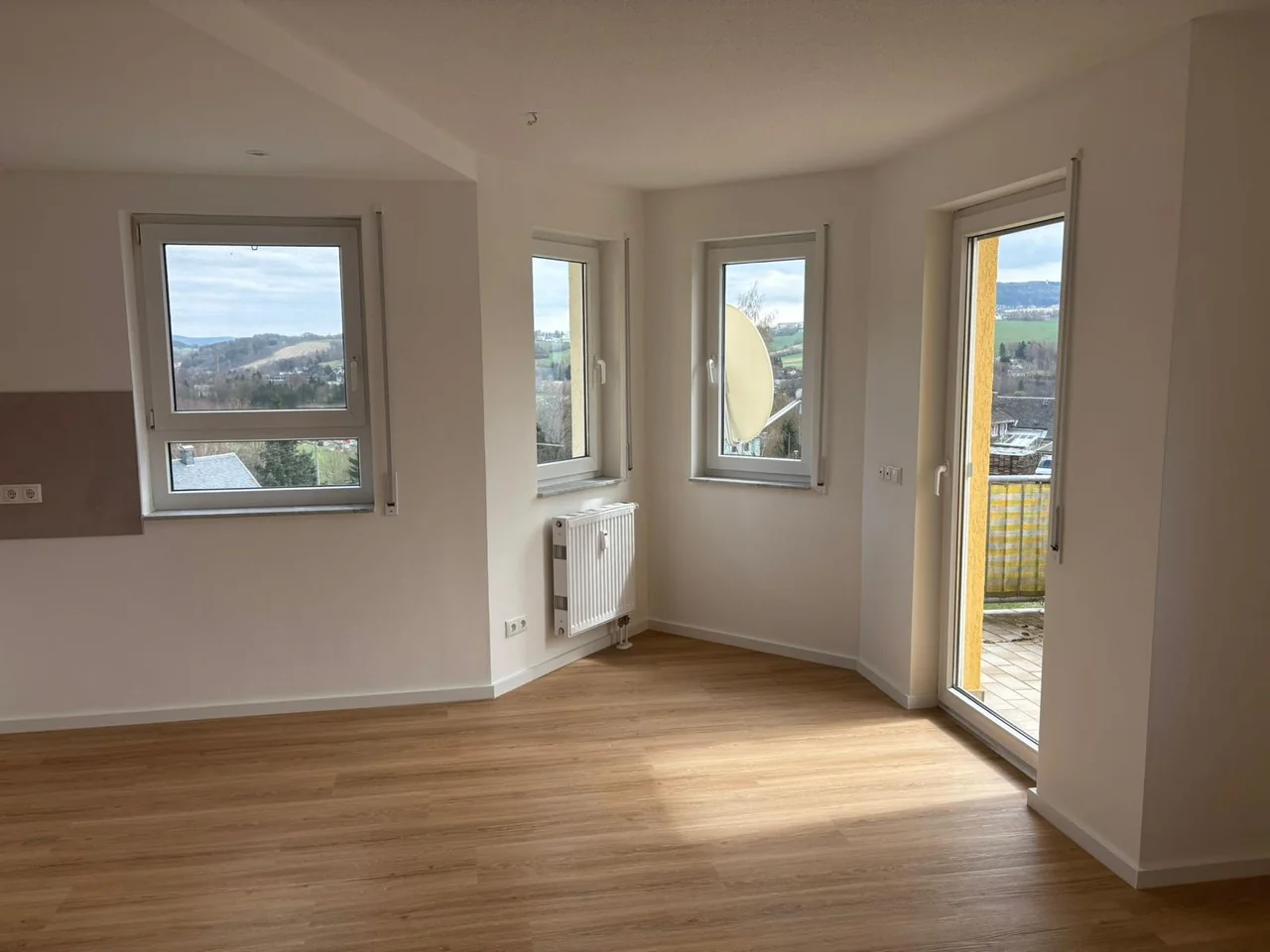Sanierter Wohnraum mit hellen Wänden, Boden in Holzoptik und Zugang zum Balkon